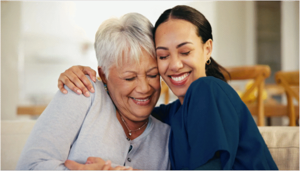 An elderly woman with gray hair is warmly embracing a younger woman, both smiling with closed eyes, conveying a sense of deep affection and happiness.
